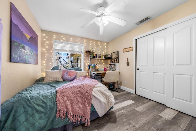 bedroom with a ceiling fan, wood finished floors, visible vents, baseboards, and a closet