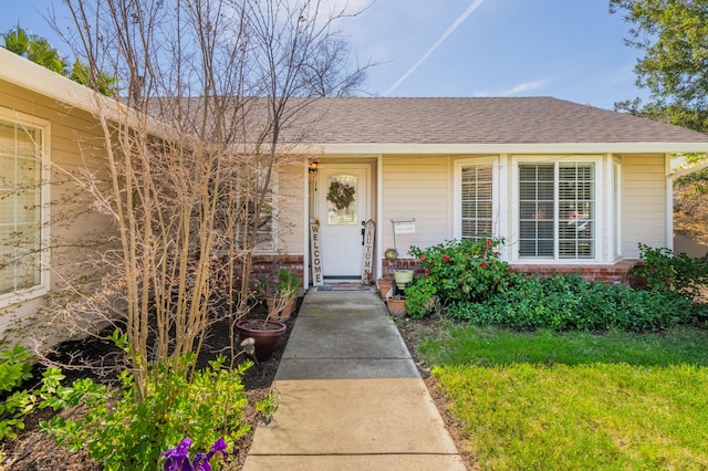 doorway to property featuring brick siding and roof with shingles