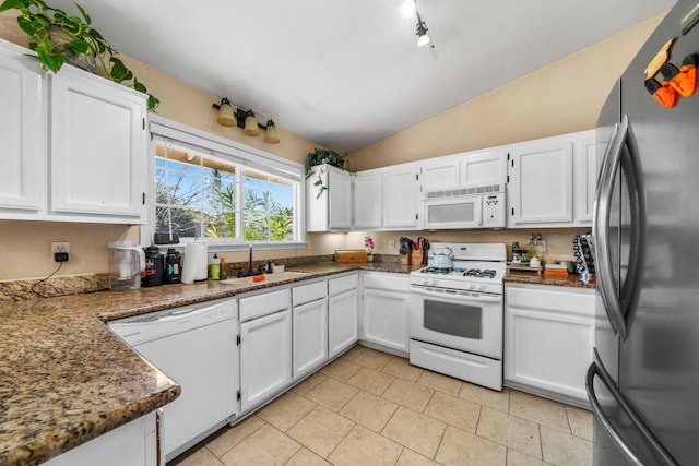 kitchen with lofted ceiling, dark stone countertops, white appliances, white cabinetry, and a sink