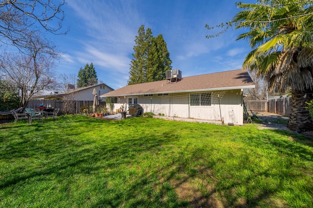 rear view of property with central AC unit, a yard, and a fenced backyard