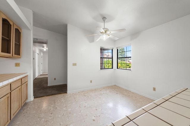 kitchen featuring light floors, baseboards, a ceiling fan, and tile counters