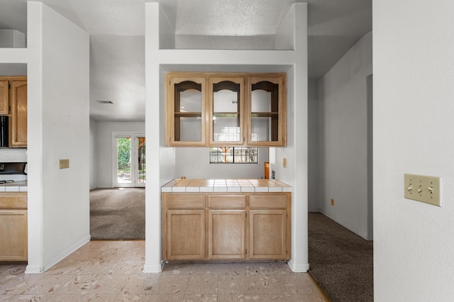 kitchen featuring glass insert cabinets, tile countertops, light colored carpet, and baseboards