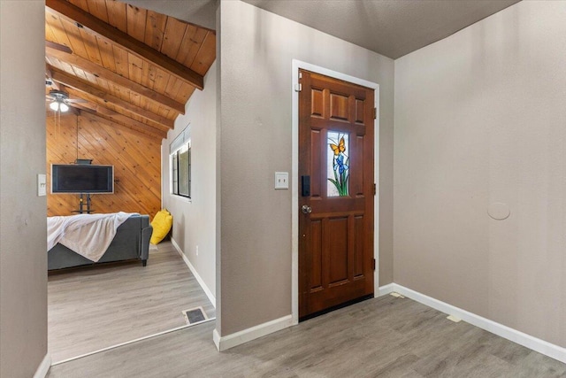 foyer entrance featuring visible vents, baseboards, wood walls, light wood-style flooring, and wooden ceiling