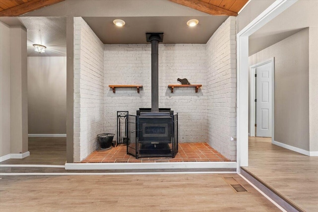 details with beam ceiling, visible vents, a wood stove, and wood finished floors