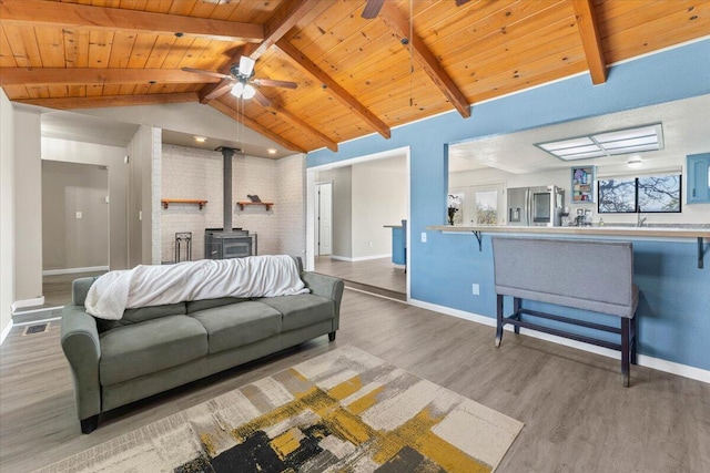 living room with lofted ceiling with beams, wood finished floors, wood ceiling, ceiling fan, and a wood stove