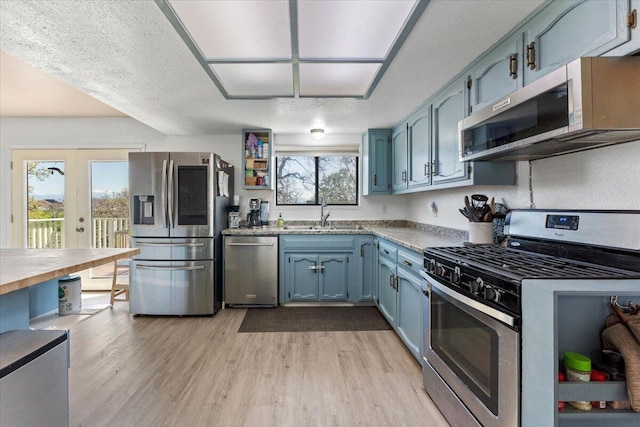 kitchen featuring a sink, blue cabinets, light wood-type flooring, and stainless steel appliances