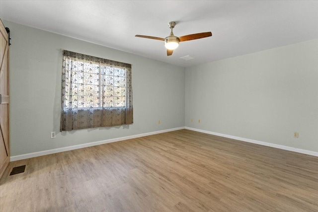 unfurnished room with visible vents, wood finished floors, a barn door, baseboards, and ceiling fan