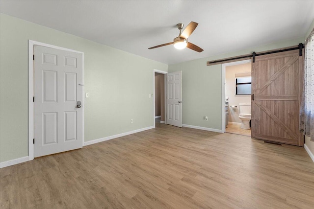 unfurnished bedroom featuring a barn door, light wood-style flooring, and baseboards