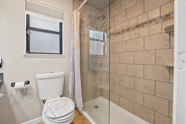 bathroom featuring tile patterned flooring, toilet, baseboards, and a tile shower