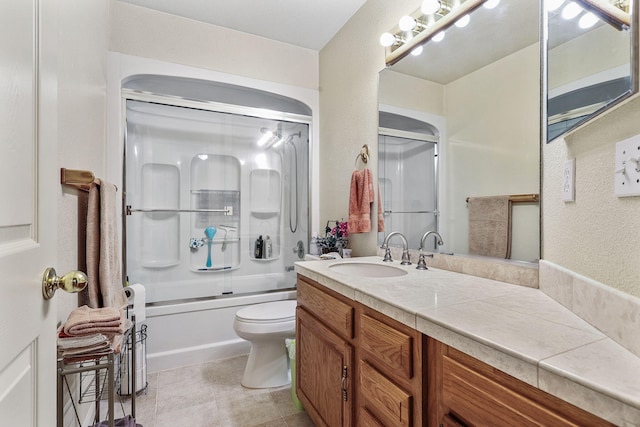 bathroom featuring bath / shower combo with glass door, toilet, a textured wall, tile patterned floors, and vanity