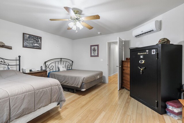bedroom featuring light wood-style flooring, a ceiling fan, and a wall unit AC