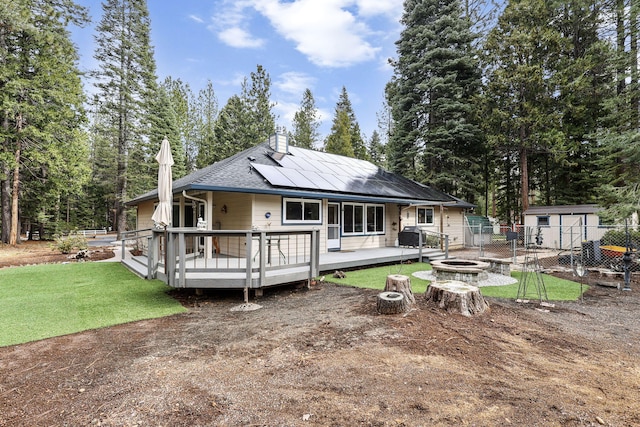 rear view of house featuring fence, a wooden deck, solar panels, an outdoor fire pit, and a lawn