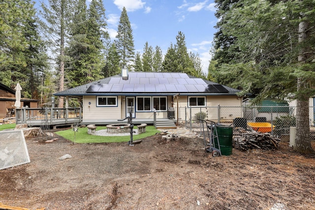 back of house with fence, a wooden deck, an outdoor fire pit, a chimney, and roof mounted solar panels