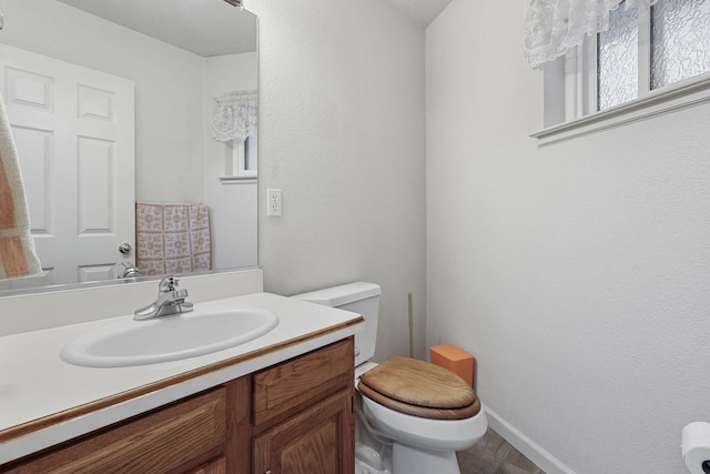 half bathroom featuring toilet, vanity, and baseboards