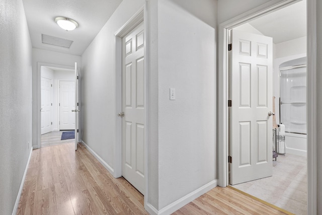 hall with attic access, light wood-style floors, baseboards, and a textured wall