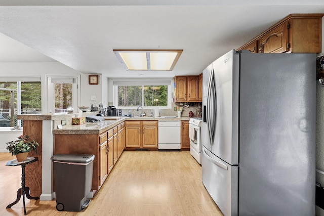 kitchen featuring light wood-style flooring, a sink, white appliances, a peninsula, and light countertops