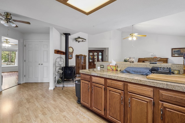 kitchen featuring a wood stove, light countertops, a ceiling fan, and light wood finished floors