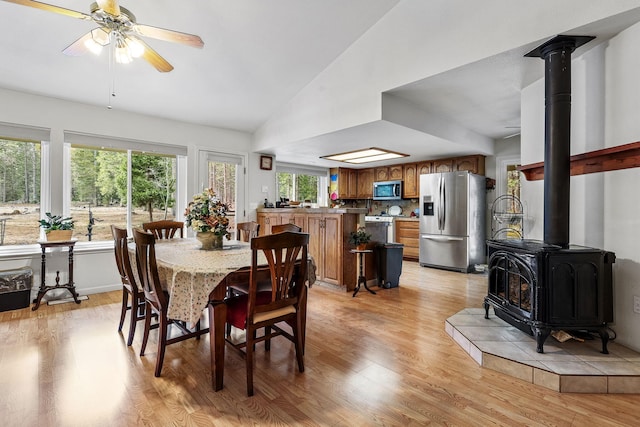 dining area featuring vaulted ceiling, a wood stove, light wood-style flooring, and ceiling fan