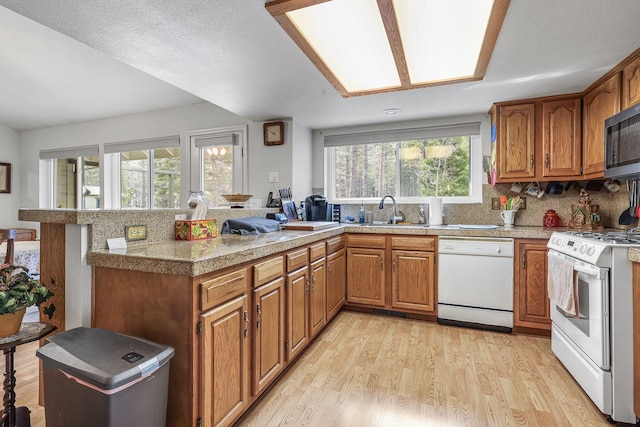 kitchen with white appliances, tile countertops, light wood finished floors, a peninsula, and a sink
