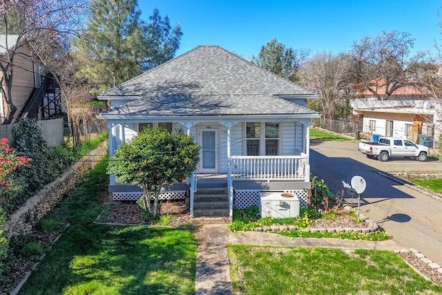bungalow-style house featuring covered porch, a front lawn, roof with shingles, and fence