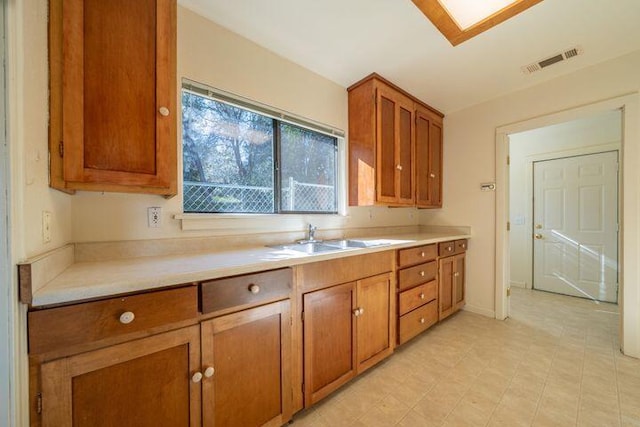 kitchen with a sink, visible vents, brown cabinets, and light countertops