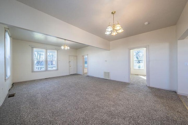 empty room with a notable chandelier, plenty of natural light, visible vents, and carpet floors