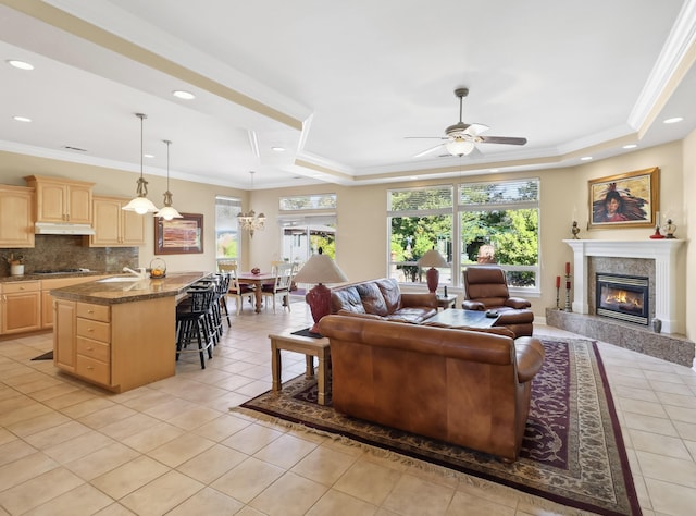 living area with a tray ceiling, crown molding, light tile patterned flooring, and a ceiling fan