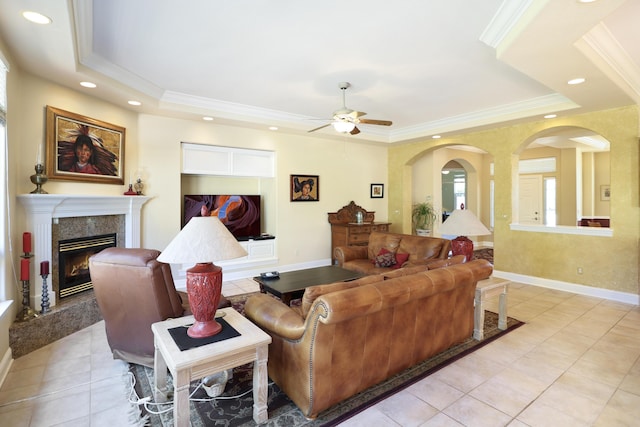 living area featuring a fireplace, a raised ceiling, a ceiling fan, and ornamental molding