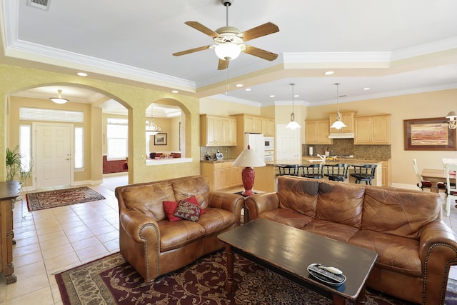 living room featuring light tile patterned flooring, arched walkways, a raised ceiling, and ceiling fan