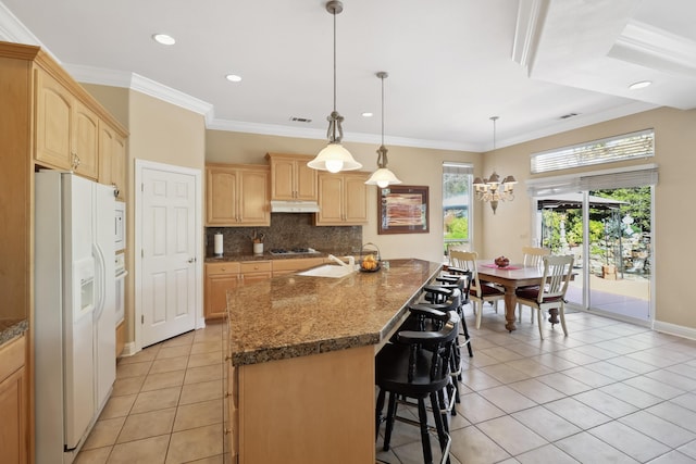 kitchen featuring white appliances, light brown cabinetry, decorative backsplash, under cabinet range hood, and a kitchen breakfast bar