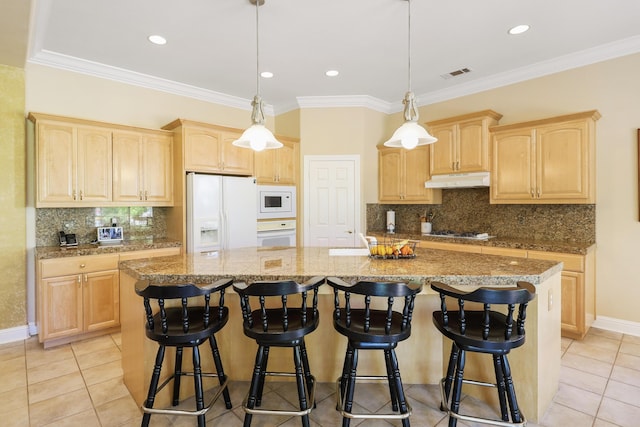 kitchen with under cabinet range hood, white appliances, a kitchen island with sink, and light brown cabinets