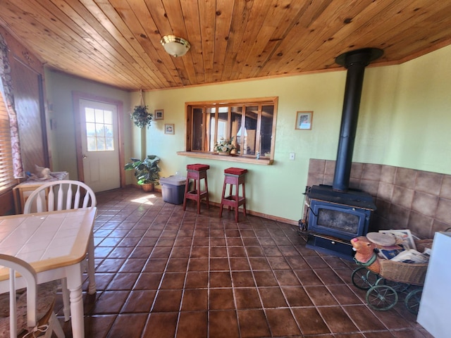 dining area with dark tile patterned floors, wood ceiling, and a wood stove