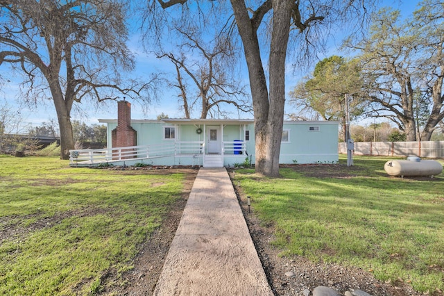 manufactured / mobile home featuring a chimney, covered porch, a front yard, and fence