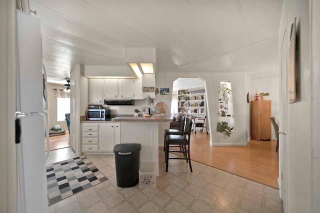 kitchen with light floors, a breakfast bar, extractor fan, white cabinets, and stainless steel microwave