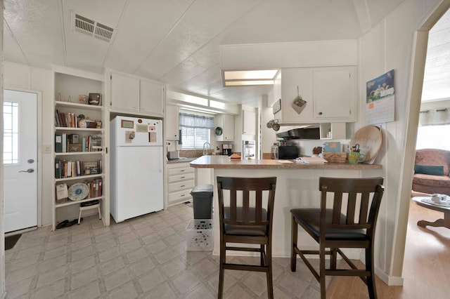 kitchen featuring visible vents, light floors, a peninsula, freestanding refrigerator, and open shelves