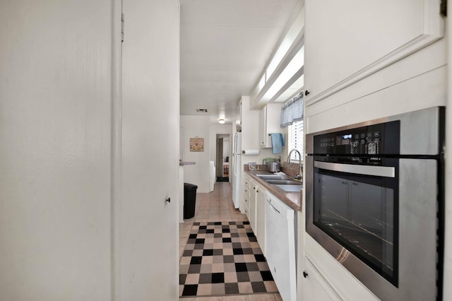 kitchen with a sink, white cabinets, dishwasher, and stainless steel oven