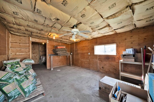 interior space with wooden walls, a ceiling fan, and concrete floors