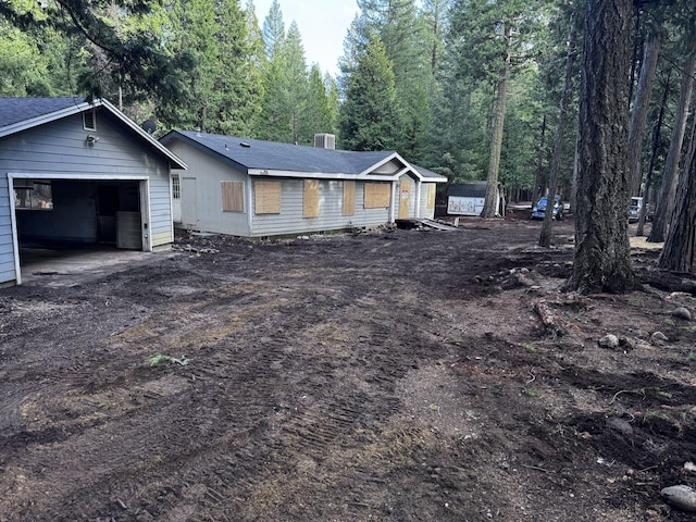 view of front of house featuring a garage, an outdoor structure, dirt driveway, and a wooded view