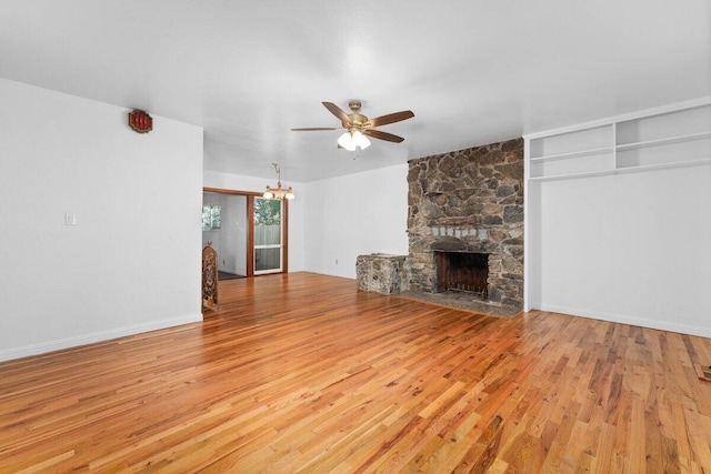 unfurnished living room featuring a stone fireplace, ceiling fan with notable chandelier, light wood-type flooring, and baseboards