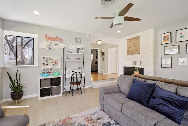 living area with wood finished floors, baseboards, visible vents, a fireplace, and ceiling fan