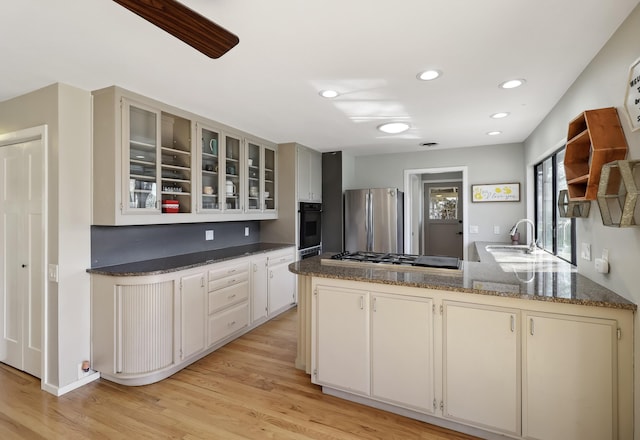 kitchen with a peninsula, a sink, glass insert cabinets, appliances with stainless steel finishes, and light wood-type flooring