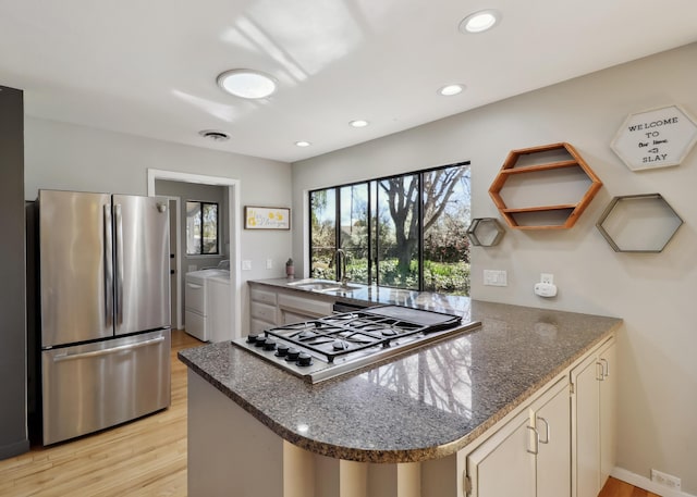 kitchen with visible vents, a peninsula, a sink, stainless steel appliances, and independent washer and dryer