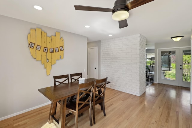 dining room with light wood-type flooring, a ceiling fan, french doors, brick wall, and baseboards