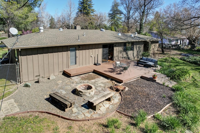 back of property featuring board and batten siding, a shingled roof, an outdoor living space with a fire pit, fence, and a wooden deck