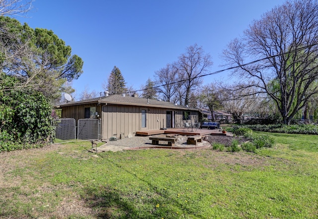 rear view of house featuring a lawn, a gate, fence, a fire pit, and board and batten siding