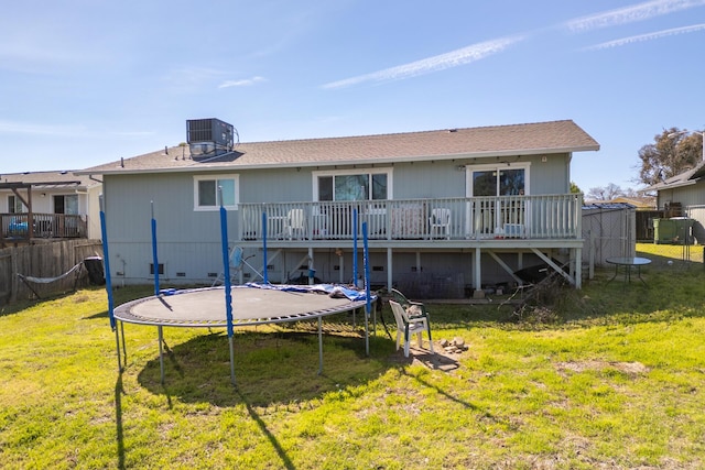 rear view of house with central air condition unit, a lawn, a trampoline, and fence