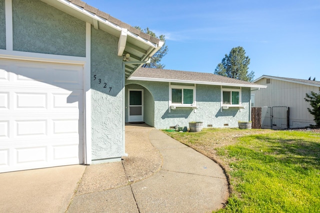 doorway to property featuring stucco siding, a garage, a yard, roof with shingles, and crawl space