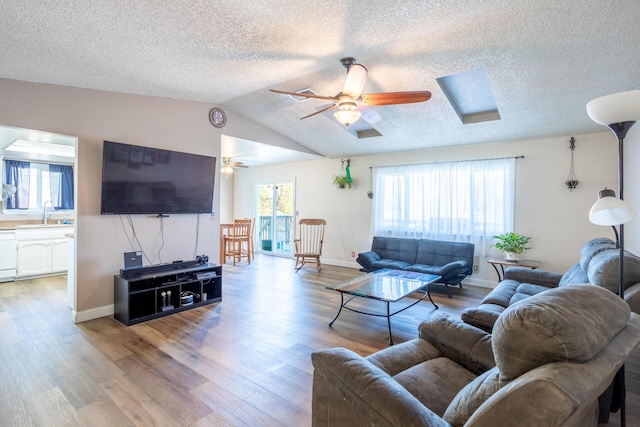 living room featuring lofted ceiling, light wood-style floors, ceiling fan, and a textured ceiling