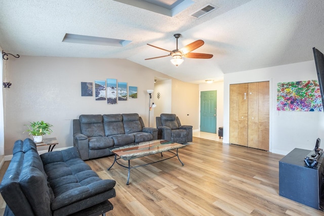 living area featuring visible vents, ceiling fan, lofted ceiling, light wood-style flooring, and a textured ceiling