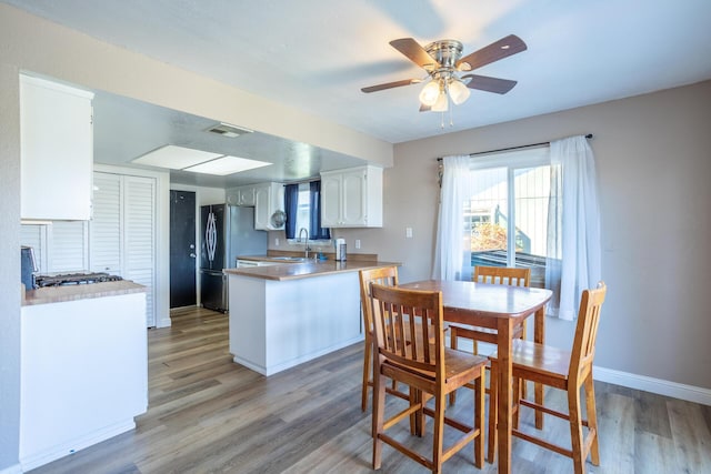 kitchen featuring visible vents, a peninsula, freestanding refrigerator, light wood-style floors, and a sink